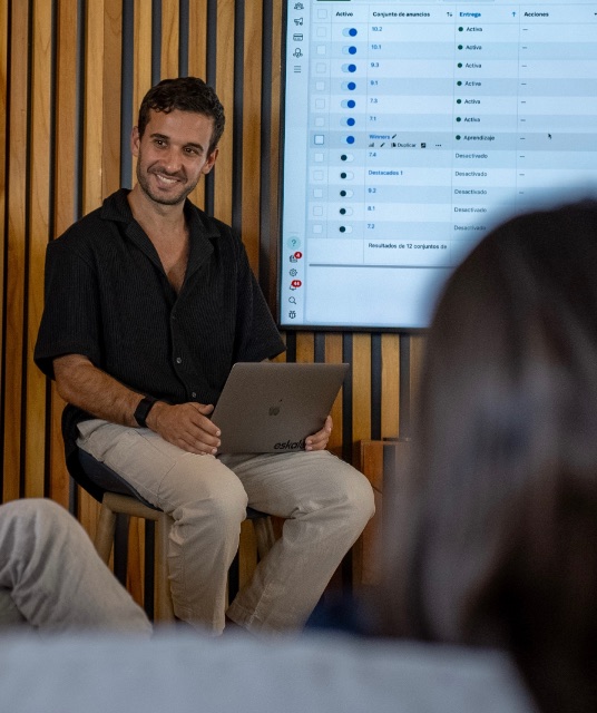 Nico Seoane sentado con su notebook, frente a una pantalla con el administrador de anuncios de Meta